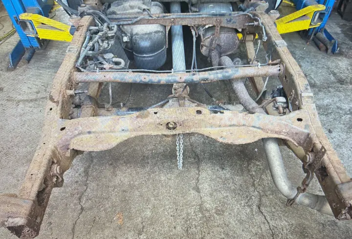 A pickup’s rear frame on the shop floor, rusted through at the rails and crossmember