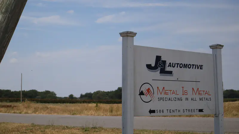 The J&L Automotive and Metal Is Metal road sign pointing to 586 Tenth Street, open fields behind it